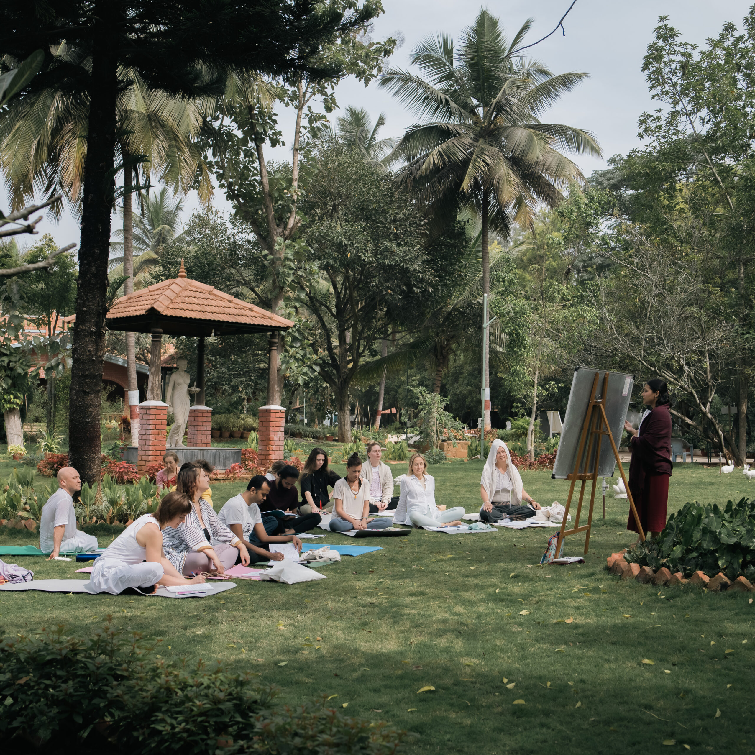 Outdoor yoga class on the lawn with students on mats and a teacher at a flipchart