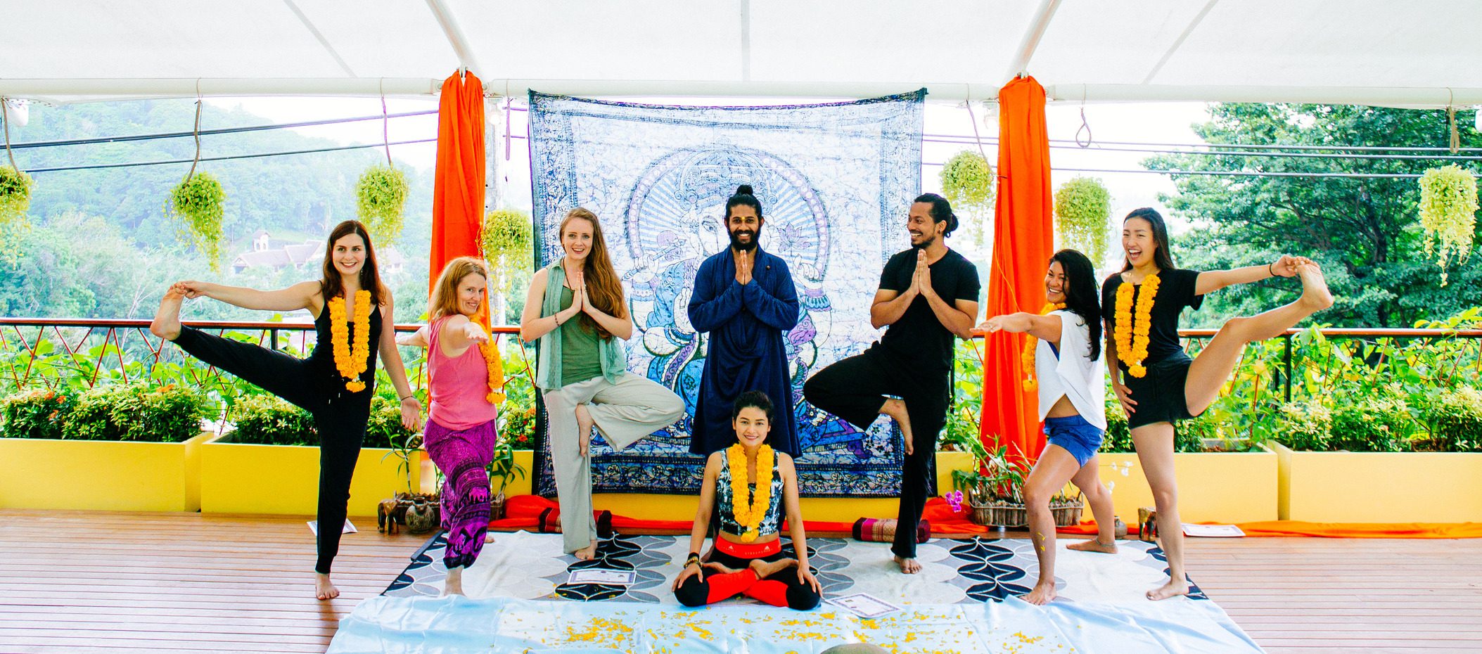 Group of yoga teacher training thailand graduates in tree pose at their graduation ceremony, marigold garlands.