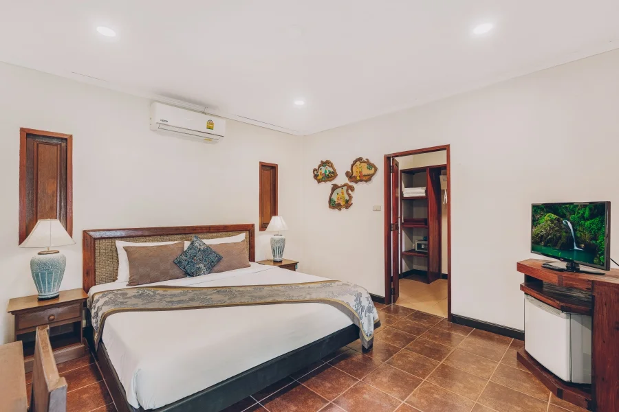 Deluxe room with wood-framed bed, flat-screen TV, mini fridge, and warm tile flooring.