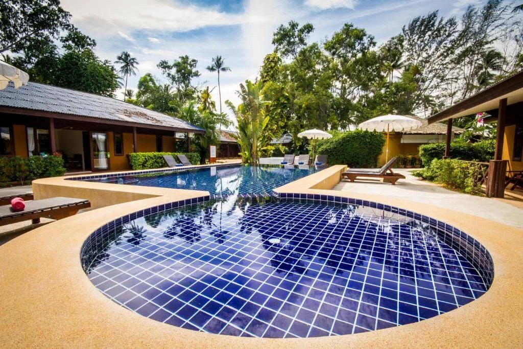 Resort pool with a round plunge pool, lap pool, sun loungers and palms.
