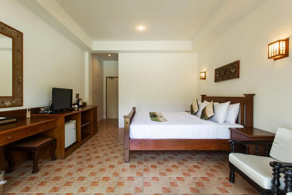Standard room with a wood-framed bed, TV console, and warm tiled floor.