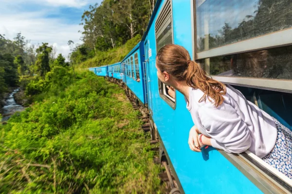 Passenger looking out of a blue train window as it passes through green hills in Sri Lanka
