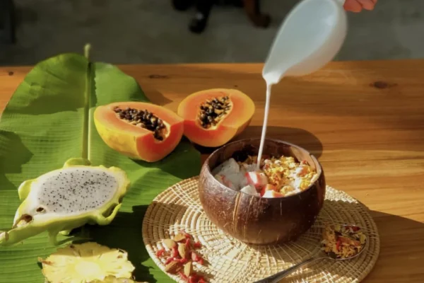 Coconut-shell bowl of granola and fruit with coconut milk being poured over the top.