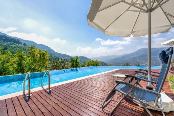 Poolside deck with sun loungers, a parasol and a mountain view