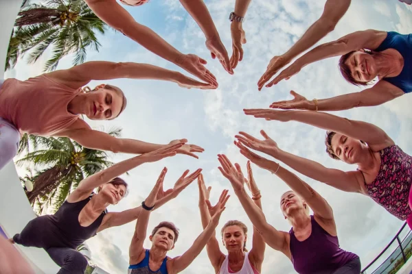 Fisheye view of a yoga group reaching their hands together overhead in a circle.