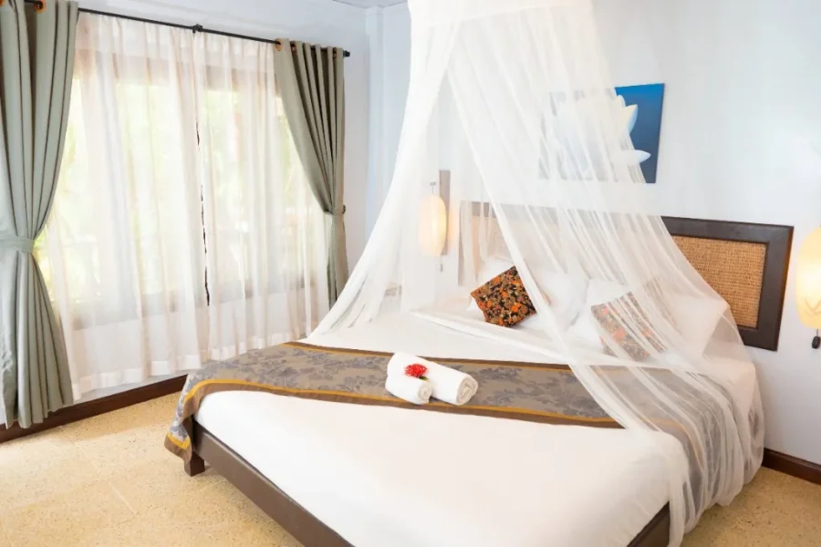 Standard room with a wood-framed bed, TV console, and warm terracotta tile flooring.